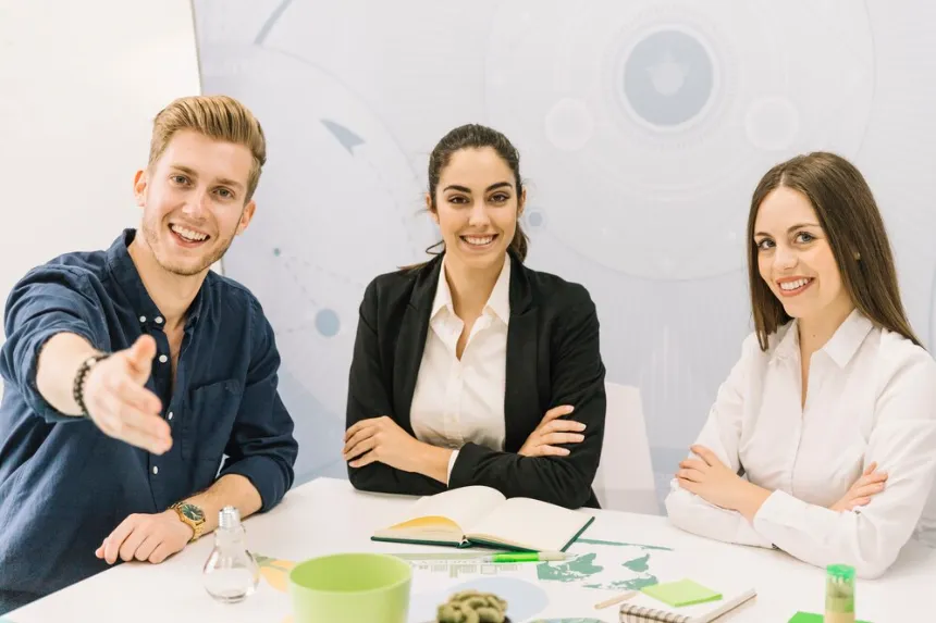 Three business professionals smiling and extending a welcoming gesture at a business directory office meeting